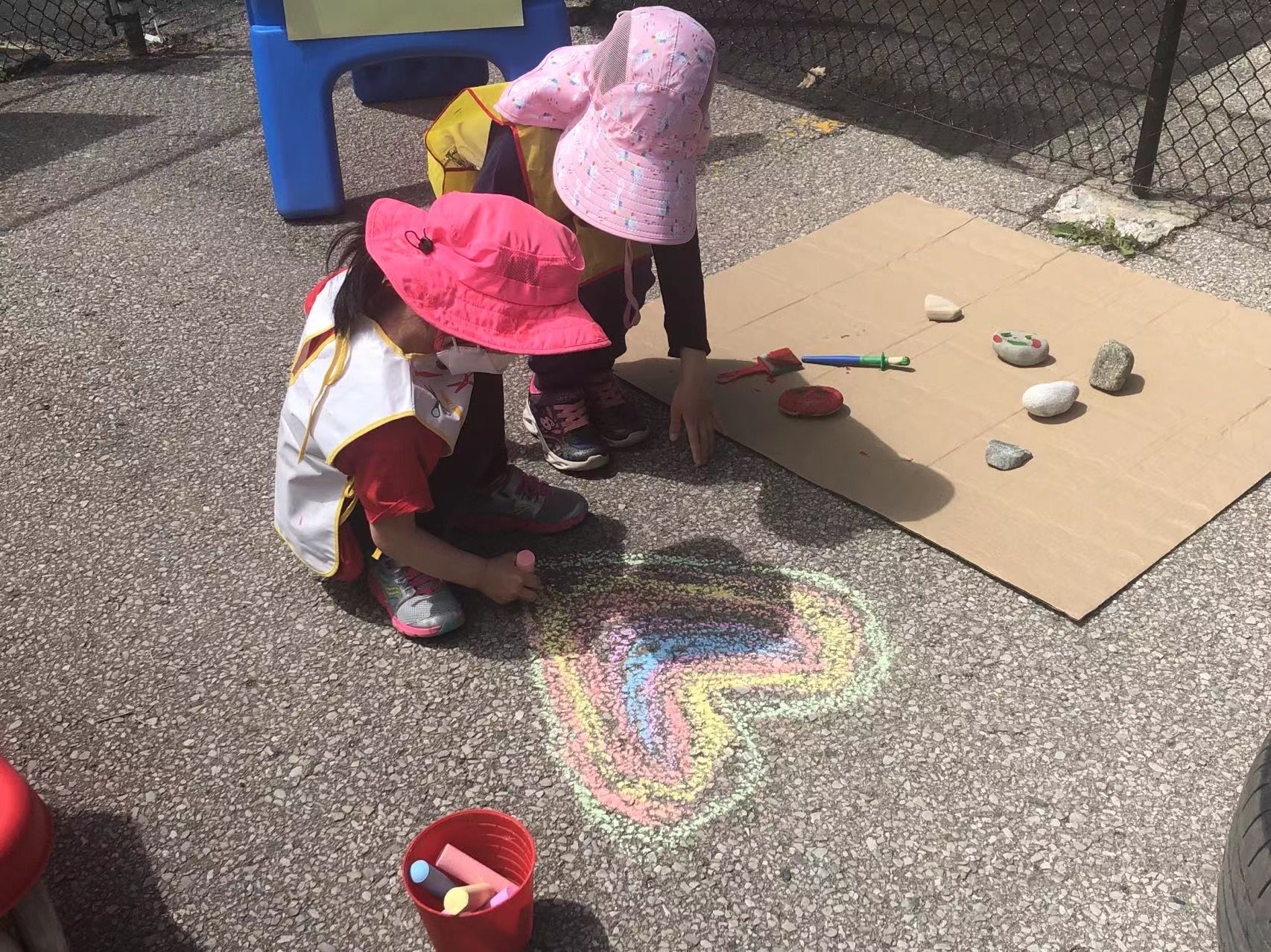 Two children in sun hats drawing with chalk on the playground
